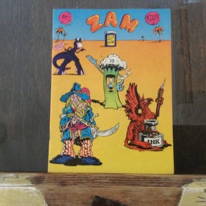May include: A vintage comic book cover with the word "ZAM" in orange letters. The illustration features cartoon characters, including a pirate, a tree-like figure, and a red winged creature with a quill and inkwell. The background is yellow with a blue sky.
