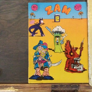 May include: A vintage comic book cover with the word "ZAM" in large letters. The illustration features several cartoon characters, including a pirate, a tree-like figure, and a red griffin with a quill and inkwell. The background is yellow and blue.