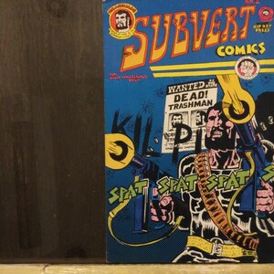 May include: Comic book cover featuring a muscular character with a machine gun, set against a blue background. The title "SUBVERT COMICS" is in yellow and orange. The cover includes the text "WANTED DEAD! TRASHMAN".
