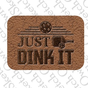 May include: A brown leather patch with the text "JUST DINK IT" in a dark brown font. The text is above a silhouette of a pickleball paddle and ball.