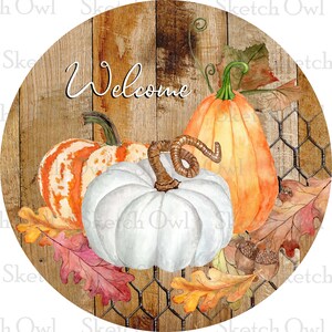 May include: A round wooden sign with a rustic woodgrain background and a wire mesh overlay. The sign features the word "Welcome" in a handwritten font and three pumpkins: one white, one orange, and one with orange and white stripes. The pumpkins are surrounded by autumn leaves in shades of red, orange, and yellow.