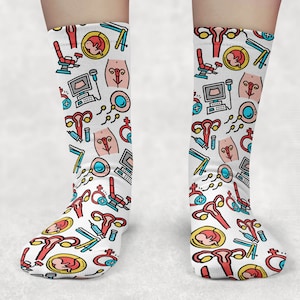 May include: A pair of white socks with a colorful pattern of medical illustrations. The pattern includes images of a uterus, ovaries, fallopian tubes, and a fetus. The socks are a fun and quirky way to show your support for women's health.