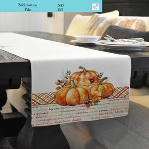 May include: A white table runner with a fall-themed design featuring three orange pumpkins with plaid and floral accents. The runner has a plaid border with text that reads "fall is in the air, pumpkin kisses, happy harvest, thankful".