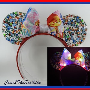 May include: Light-up Minnie Mouse ears with a colorful bow and a Christmas-themed design. The ears are decorated with glitter and rhinestones. The bow features a character from the movie "Frozen".