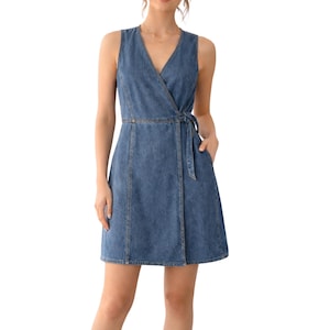 May include: Sleeveless denim wrap dress in a medium blue wash. The dress features a V-neckline, a waist tie, and two front pockets. The dress has a knee-length hemline and is made of a sturdy denim fabric.