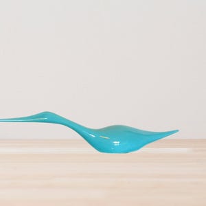 May include: A turquoise blue ceramic bird sculpture with a long neck and a slender body. The bird is in a resting position with its head tilted slightly to the side.