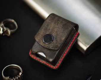 May include: A black leather case with red stitching and a metal button closure. The case is designed to hold a small object, such as a lighter or a pocket knife.