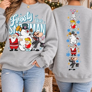 May include: A light grey crewneck sweatshirt featuring a graphic print of Frosty the Snowman, Santa Claus, and other characters on the front with the text Frosty the Snowman. The back displays a vertical column of the same characters and snowflakes.
