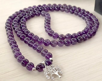 May include: A purple amethyst mala necklace with a silver tree of life charm. The necklace is made of 8mm beads and is approximately 18 inches long.