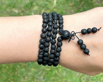 May include: A black lava rock beaded bracelet with a knotted tassel. The bracelet is worn on a person's wrist.