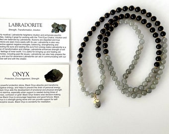 Può includere: Un collana mala con perline nere e grigie con un ciondolo in labradorite. La collana è realizzata con perline di onice nero e labradorite. Le schede descrivono le proprietà della labradorite e dell'onice.