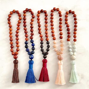 May include: Five strands of prayer beads, each featuring a series of round wooden beads and a decorative tassel. The strands incorporate various accent beads in colours including deep blue, dark brown, pale peach, and light mint green.