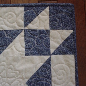 Puede incluir: Una colcha con un dise&ntilde;o de patchwork que presenta cuadrados alternos de tela blanca con un patr&oacute;n de espiral y tela azul con un peque&ntilde;o estampado floral. La colcha est&aacute; hecha con una variedad de telas y tiene un dise&ntilde;o &uacute;nico e intrincado.