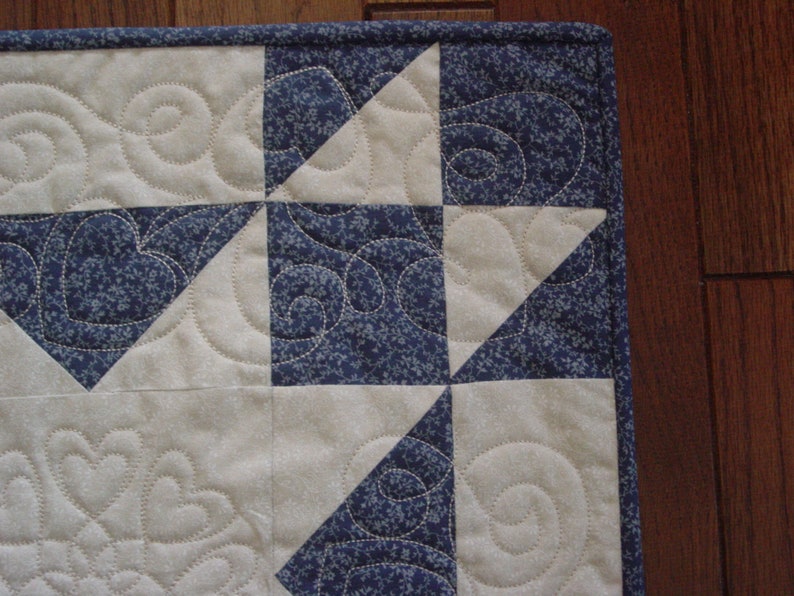 Puede incluir: Una colcha con un dise&ntilde;o de patchwork que presenta cuadrados alternos de tela blanca con un patr&oacute;n de espiral y tela azul con un peque&ntilde;o estampado floral. La colcha est&aacute; hecha con una variedad de telas y tiene un dise&ntilde;o &uacute;nico e intrincado.