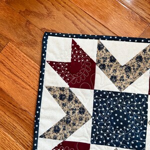 May include: A quilt with a star pattern in red, white, and blue fabric. The quilt is made with a variety of fabrics, including floral prints and solid colors. The quilt is edged with a white trim.