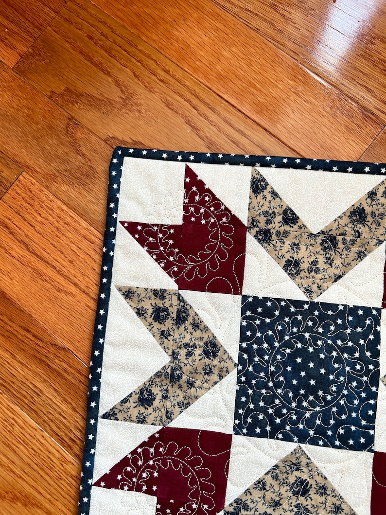May include: A quilt with a star pattern in red, white, and blue fabric. The quilt is made with a variety of fabrics, including floral prints and solid colors. The quilt is edged with a white trim.