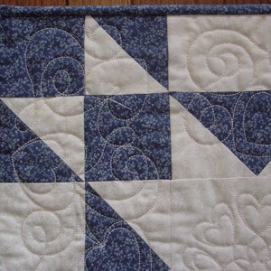 Puede incluir: Primer plano de una colcha con un patr&oacute;n floral azul y blanco. La colcha est&aacute; hecha de cuadrados y tri&aacute;ngulos, y las costuras son visibles. La colcha est&aacute; acolchada con un patr&oacute;n de espiral.