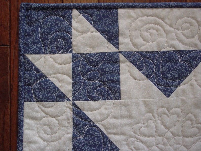 Puede incluir: Primer plano de una colcha con un patr&oacute;n floral azul y blanco. La colcha est&aacute; hecha de cuadrados y tri&aacute;ngulos, y las costuras son visibles. La colcha est&aacute; acolchada con un patr&oacute;n de espiral.