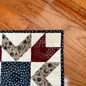 May include: A close-up of a handmade quilt with a star pattern in red, white, and blue fabrics. The quilt is made with a variety of fabrics, including floral prints and solid colors. The quilt is edged with a black and white polka dot trim.
