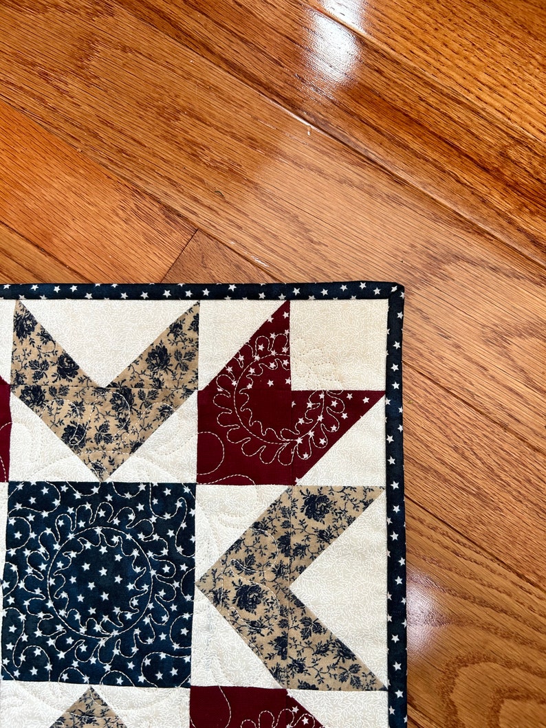 May include: A close-up of a handmade quilt with a star pattern in red, white, and blue fabrics. The quilt is made with a variety of fabrics, including floral prints and solid colors. The quilt is edged with a black and white polka dot trim.