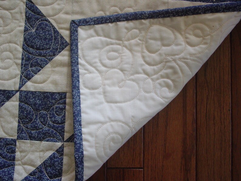 Puede incluir: Una colcha blanca con un patr&oacute;n floral azul y blanco. La colcha est&aacute; doblada por la mitad y se ve el lado de atr&aacute;s. El lado de atr&aacute;s es blanco con un borde azul y un patr&oacute;n de espiral.