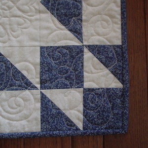 Puede incluir: Primer plano de una colcha con un patr&oacute;n geom&eacute;trico azul y blanco. La colcha est&aacute; hecha de tela con un peque&ntilde;o estampado floral. La colcha est&aacute; ribeteada con un ribete azul.