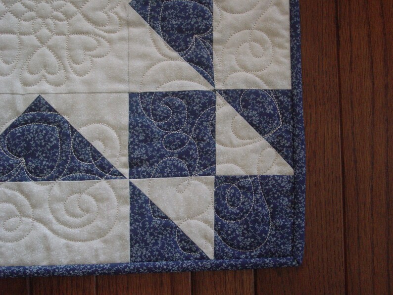 Puede incluir: Primer plano de una colcha con un patr&oacute;n geom&eacute;trico azul y blanco. La colcha est&aacute; hecha de tela con un peque&ntilde;o estampado floral. La colcha est&aacute; ribeteada con un ribete azul.