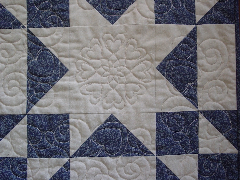Puede incluir: Una colcha con fondo blanco y cuadrados azules. Los cuadrados tienen un patr&oacute;n floral y est&aacute;n dispuestos en forma de estrella.