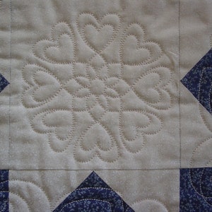 Puede incluir: Primer plano de una colcha con fondo blanco y estampado floral azul. La colcha est&aacute; acolchada con un dise&ntilde;o de coraz&oacute;n.