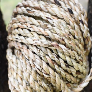 May include: A tightly coiled rope made of natural fibers, showcasing a blend of beige and brown hues. The rope is tightly wound, creating a textured surface. The image highlights the craftsmanship and natural materials.