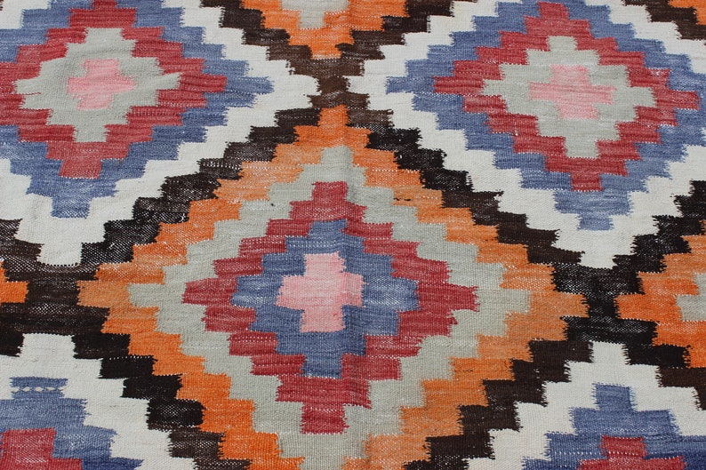 Pu&ograve; includere: Un tappeto colorato con un motivo geometrico in tonalit&agrave; di arancione, rosso, blu e bianco.
