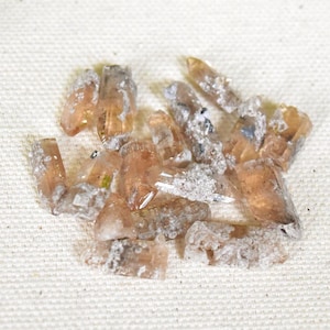 May include: A collection of raw, uncut crystals. The crystals are a translucent, light orange-brown color with some white and gray inclusions. They are irregularly shaped and appear to be natural gemstones.