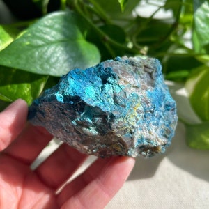 May include: A rough, blue-green and gray chrysocolla crystal with a natural, irregular shape. The crystal has a metallic sheen and is partially covered in a white, powdery substance.