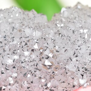 May include: Close-up of a cluster of clear quartz crystals with a silvery sheen. The crystals are densely packed together, creating a textured surface.