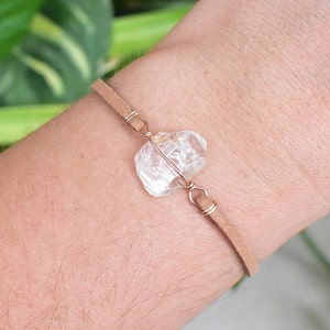May include: A tan leather bracelet with a clear quartz crystal wrapped in copper wire.
