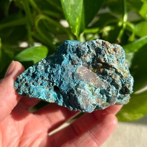 May include: A rough, teal blue and brown crystal with a white quartz inclusion. The crystal has a natural, irregular shape and a textured surface.