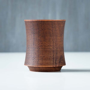 May include: A dark brown wooden cup with a ribbed design. The cup is made of wood and has a smooth, polished finish.