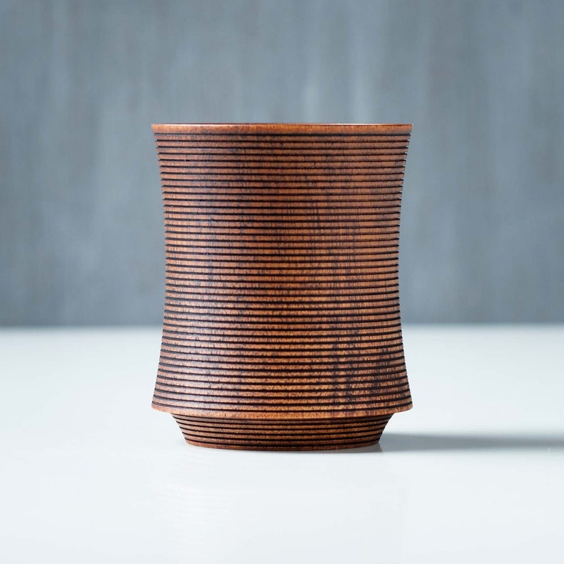 May include: A dark brown wooden cup with a ribbed design. The cup is made of wood and has a smooth, polished finish.