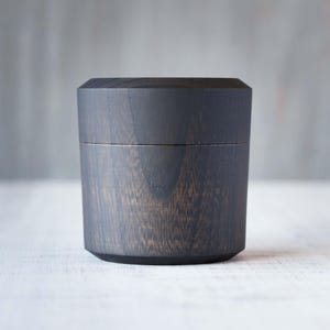 May include: A dark gray wooden box with a lid. The box has a smooth, polished finish and a slightly rounded shape.