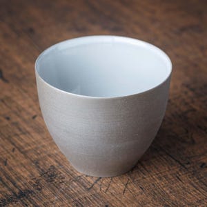 May include: A gray ceramic teacup with a white interior. The cup has a smooth, slightly textured surface.