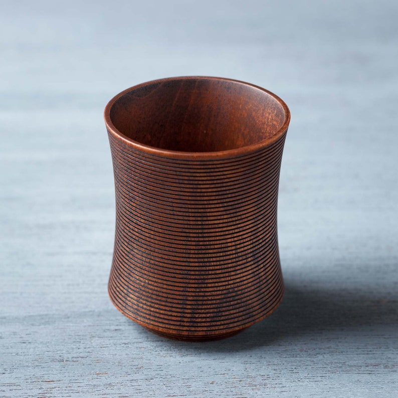 May include: A dark brown wooden cup with a ribbed design. The cup is made of wood and has a smooth, polished finish.