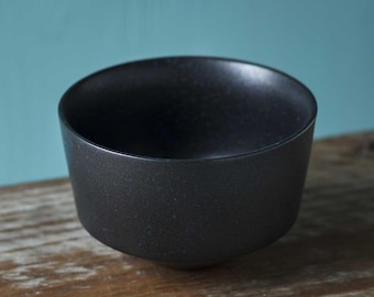 May include: A black ceramic bowl with a textured surface. The bowl is round and has a wide rim.