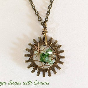 May include: Antique brass gear necklace with a green crystal in the center. The gear is surrounded by wire and the necklace has a chain.