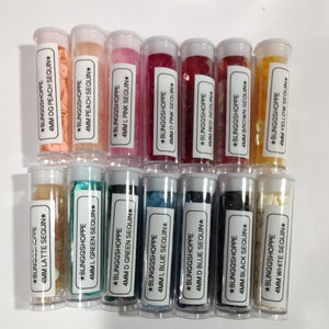 May include: Twelve small clear plastic jars filled with various colors of 4mm sequins. The jars are labeled with the color and size of the sequins.  The colors include peach, latte, green, blue, pink, red, brown, black, white, and yellow.