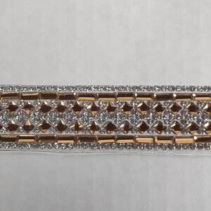 May include: A close-up of a gold and silver trim with a repeating pattern of small squares and rectangles. The trim is made of rhinestones and is perfect for adding a touch of sparkle to any project.