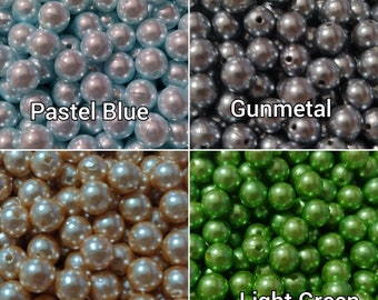 May include: Assortment of pearl beads in four colors: pastel blue, gunmetal, light gold, and light green. The beads are all the same size and have a smooth, shiny finish.