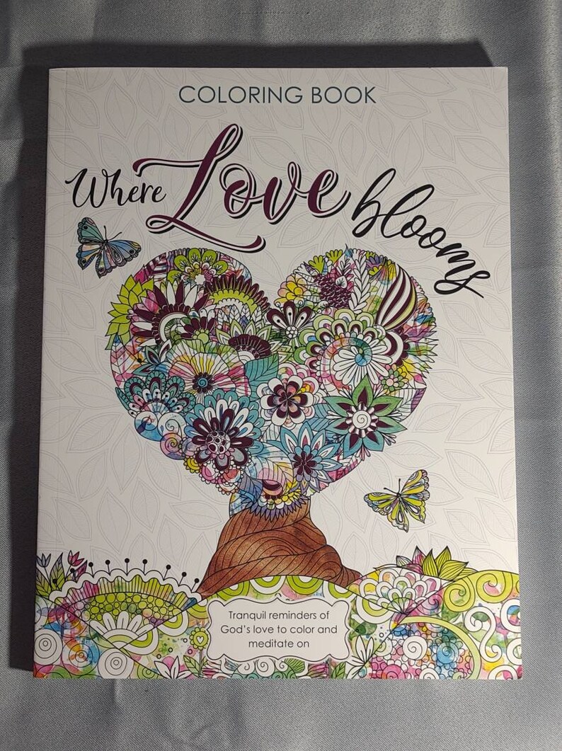 May include: A coloring book cover with a heart-shaped tree with flowers and butterflies. The title of the book is "Where Love Blooms". The text below the image says "Tranquil reminders of God's love to color and meditate on."