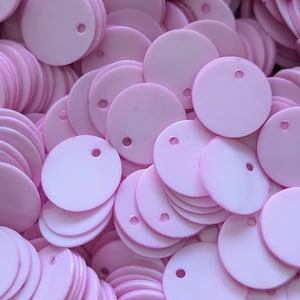 May include: A large pile of light pink round sequins with a small hole in the center of each sequin.