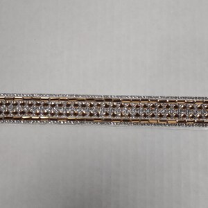 May include: A silver and gold trim with a repeating pattern of small squares. The trim is made of rhinestones and is perfect for adding a touch of sparkle to any project.
