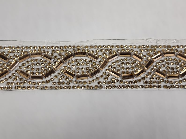May include: Gold and clear rhinestone trim with a repeating pattern of small round rhinestones and larger rectangular rhinestones.